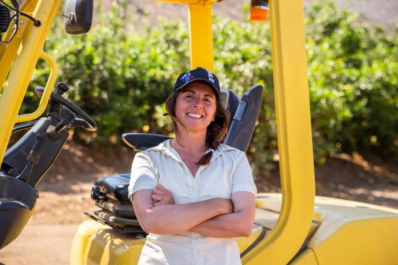 Retrato de una trabajadora de pie frente a una grúa horquilla